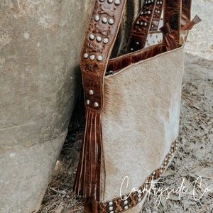 Western style cowhide leather purse with brass accents and fringe.