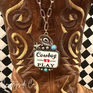 Silver cowboy hat charm necklace with turquoise and "Cowboy Play" text on boot.