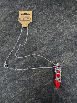 Red crystal pendant necklace with silver floral vines and a silver chain with Handmade By MLC tag on a dark wood background.