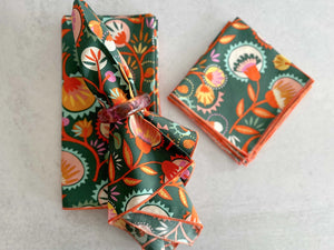 Green floral print cloth napkins with an orange border and a decorative napkin ring.