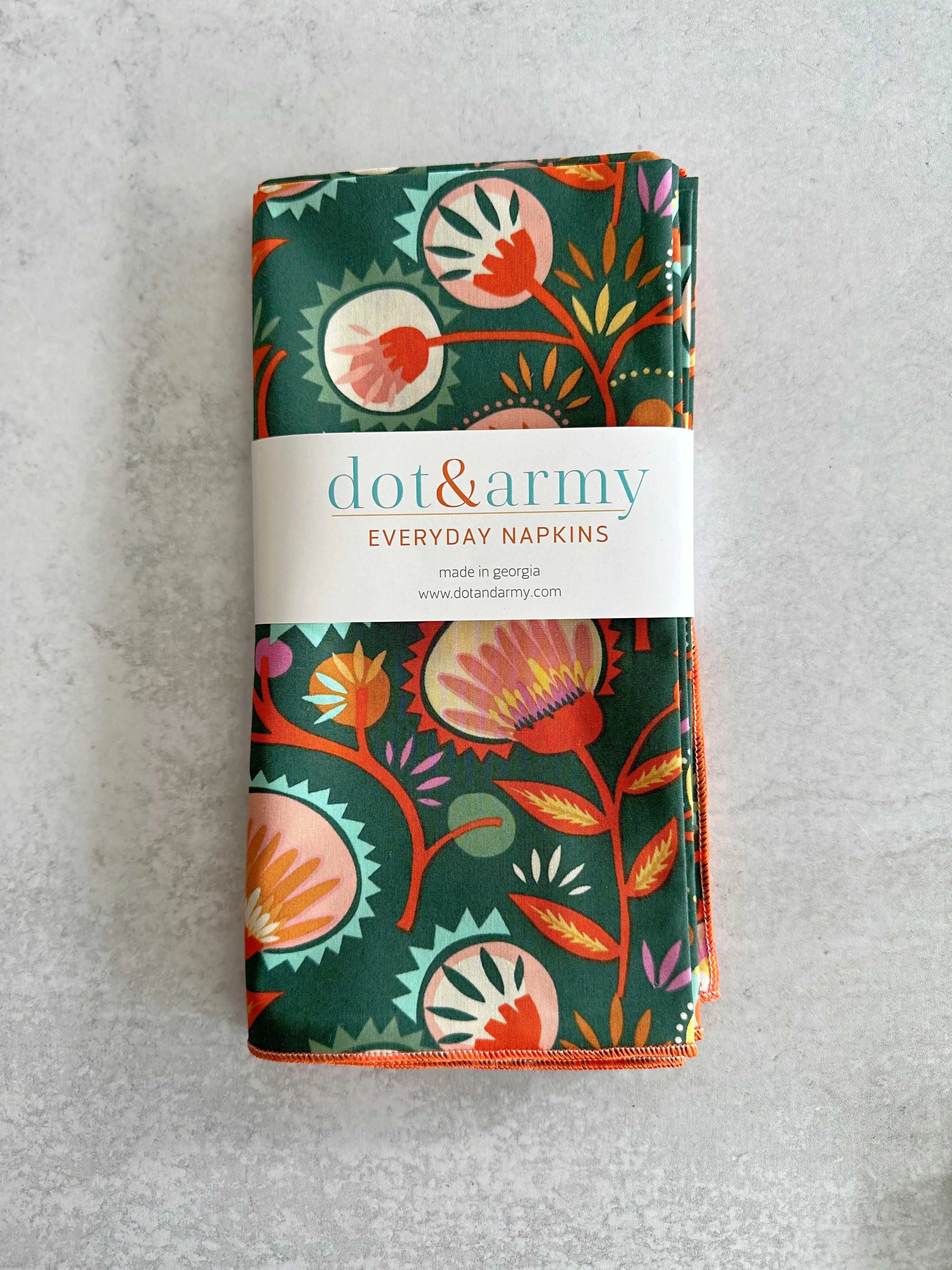 Folded dark green cotton napkins with a colorful floral pattern and a white band.