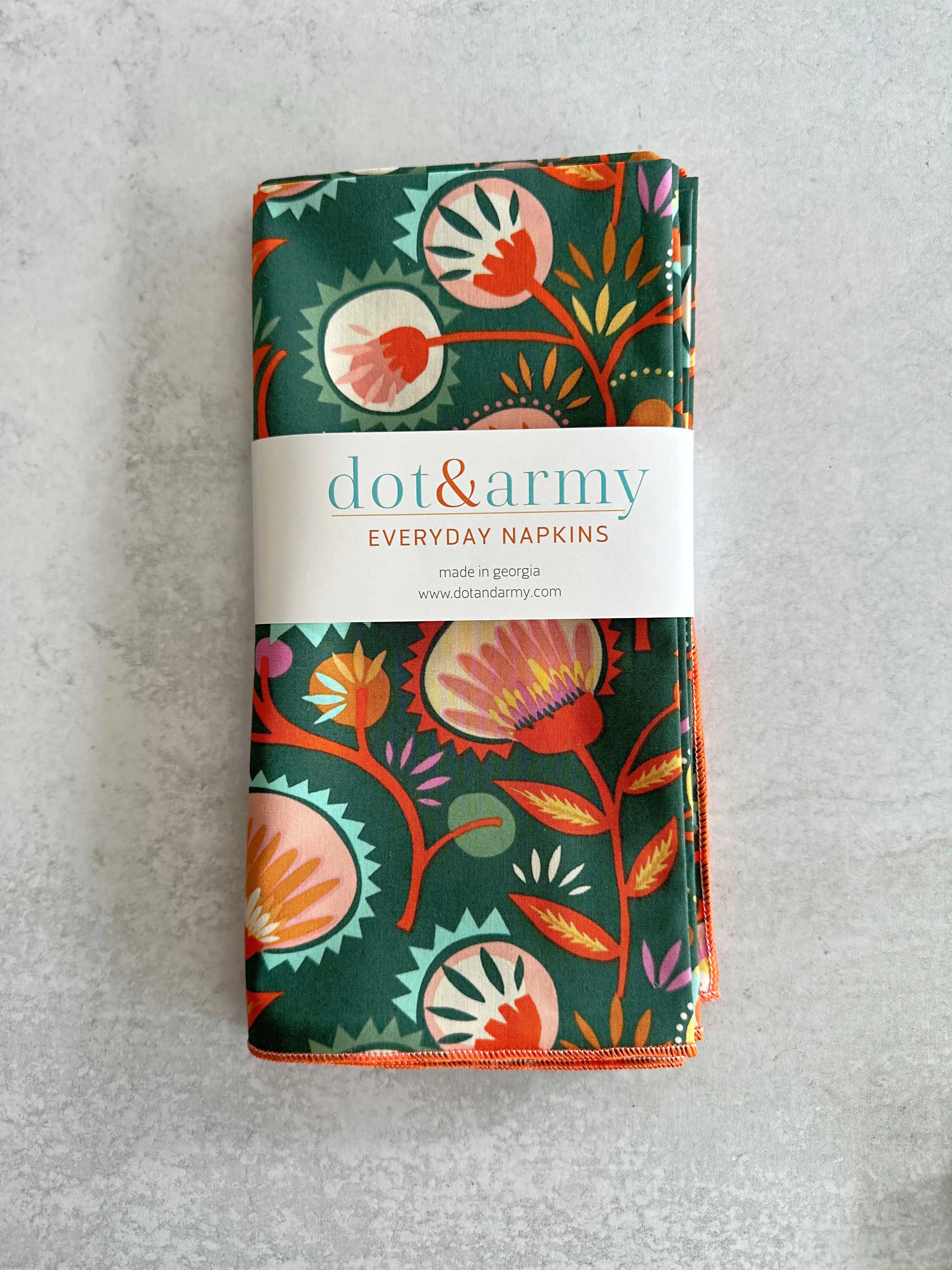 Folded dark green cotton napkins with a colorful floral pattern and a white band.