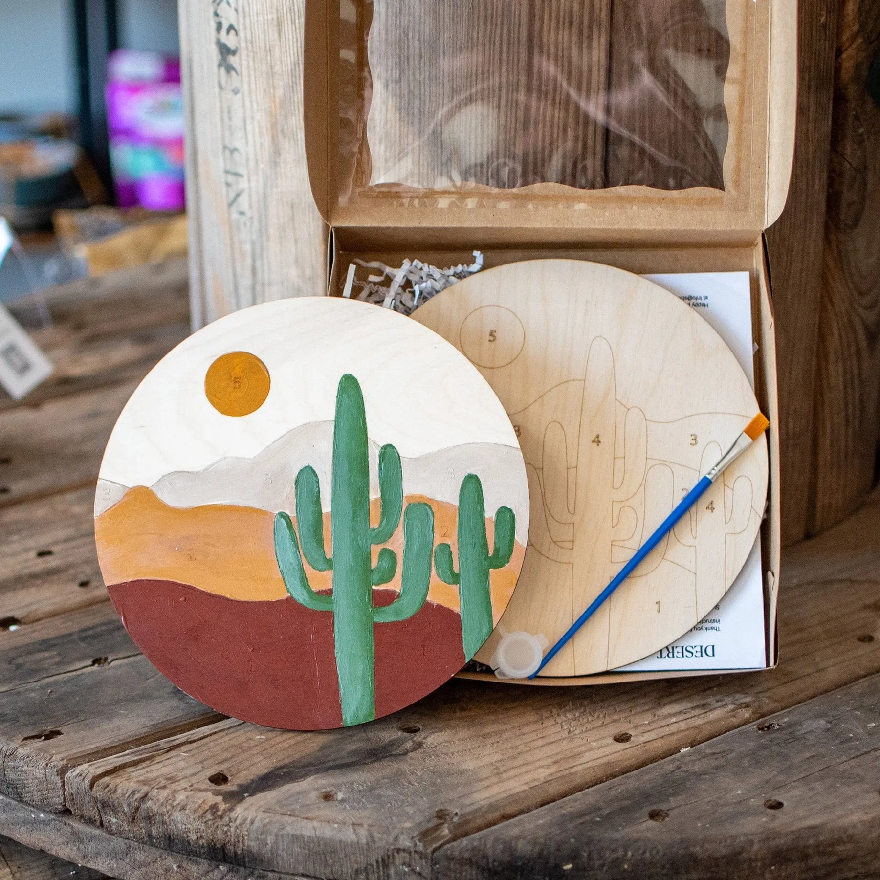 Wooden paint by number kit with desert landscape, cactus, sun, and brush.