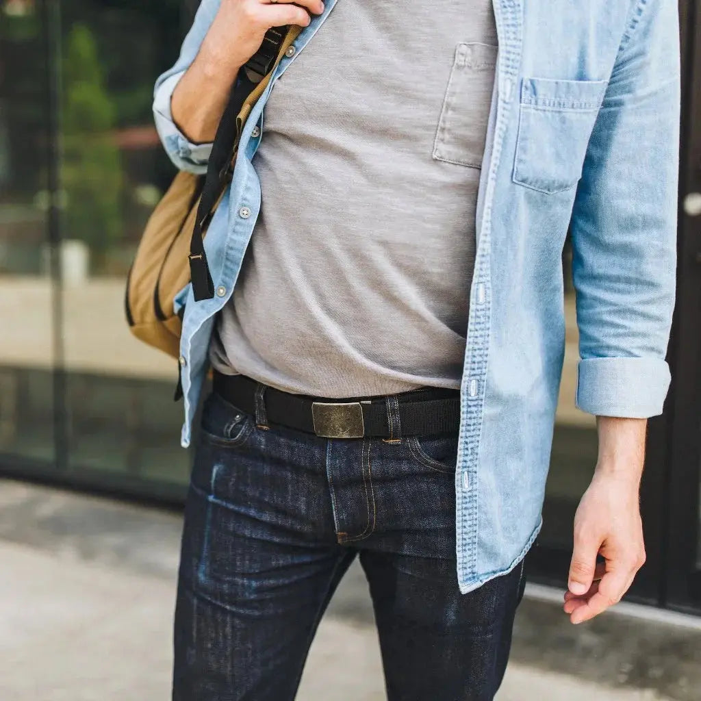 Black fabric EDC belt with brass buckle worn with dark jeans