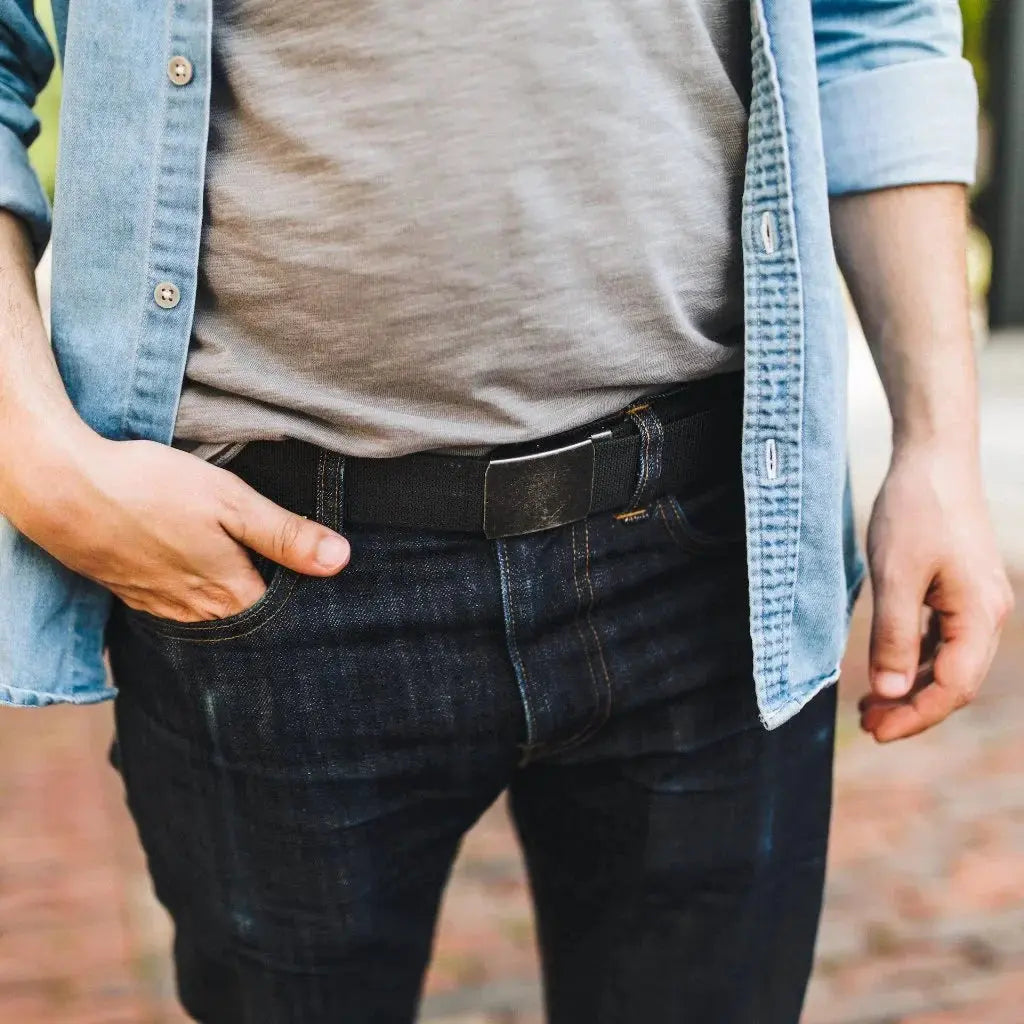 Man wearing a denim shirt, grey t-shirt, dark wash jeans, and a black EDC belt with a metal buckle.