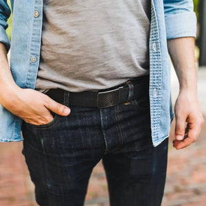 Man wearing a denim shirt, grey t-shirt, dark wash jeans, and a black EDC belt with a metal buckle.
