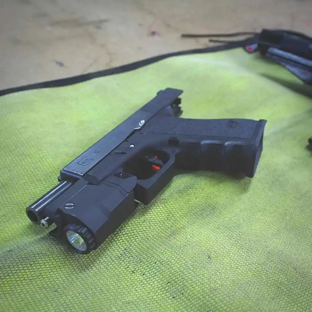 Black handgun with light attachment on a green textured mat.