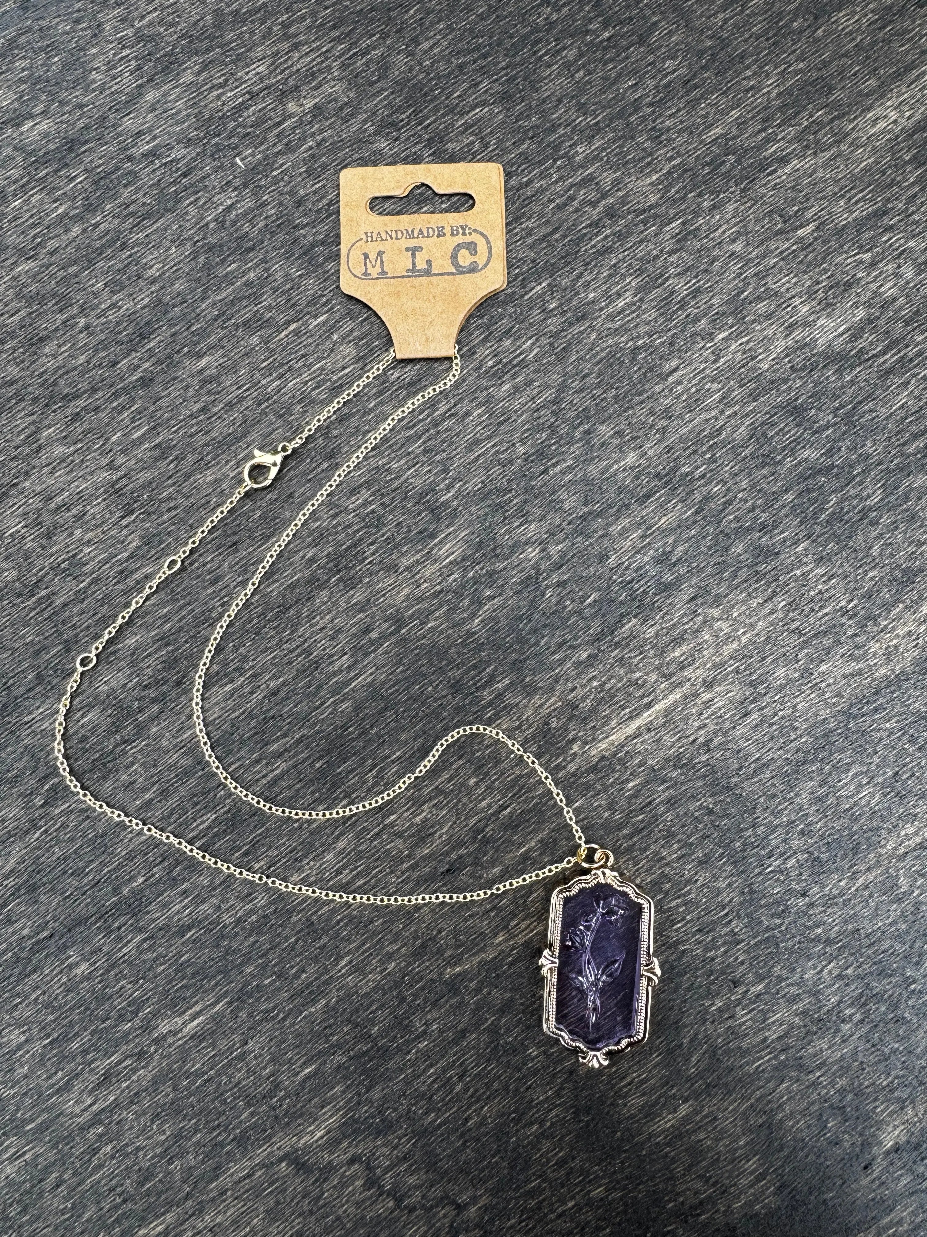 Purple glass necklace with a carved flower pendant and a silver chain. Tag reads "Handmade by: MLC".