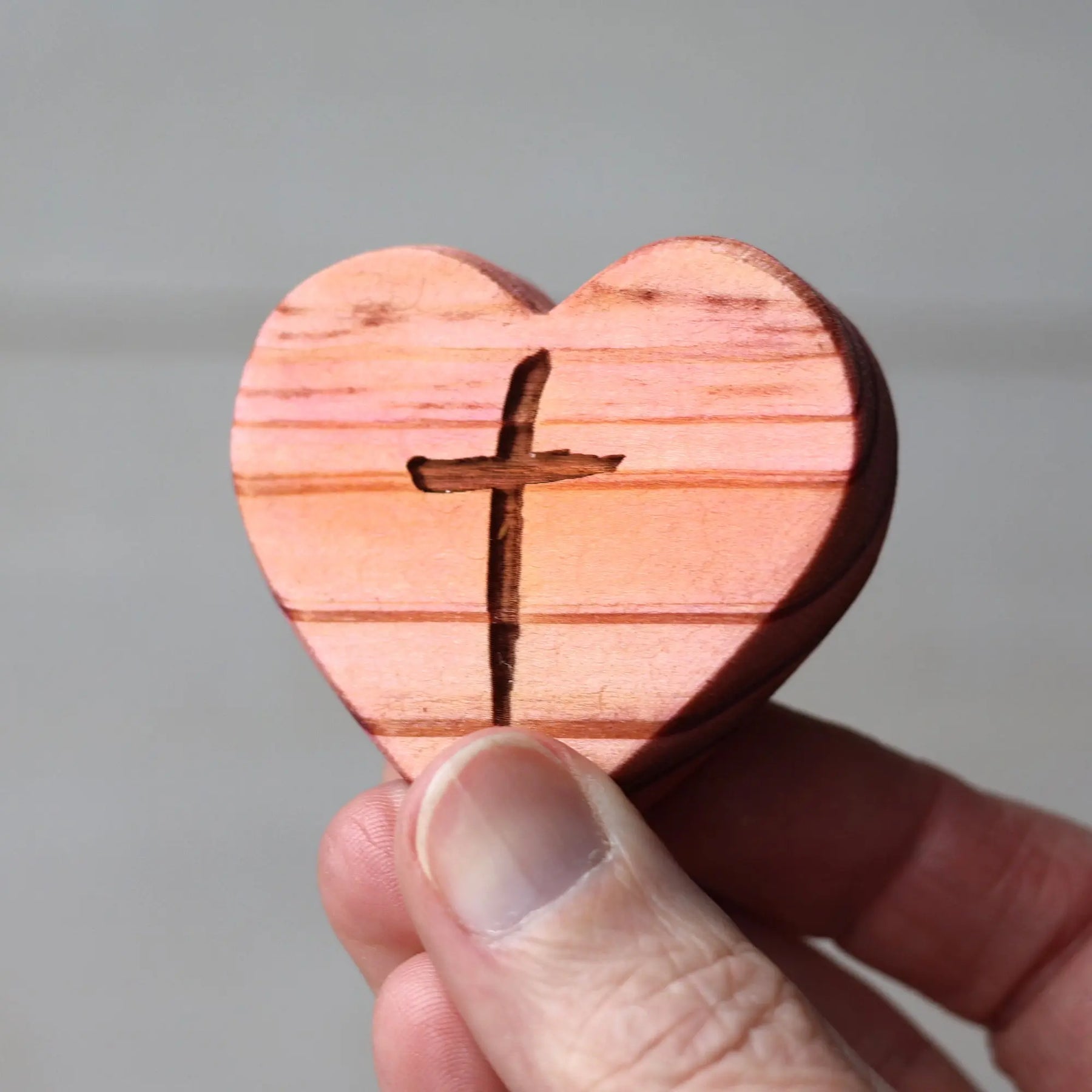 Wooden heart with a carved cross held in a person's fingers.