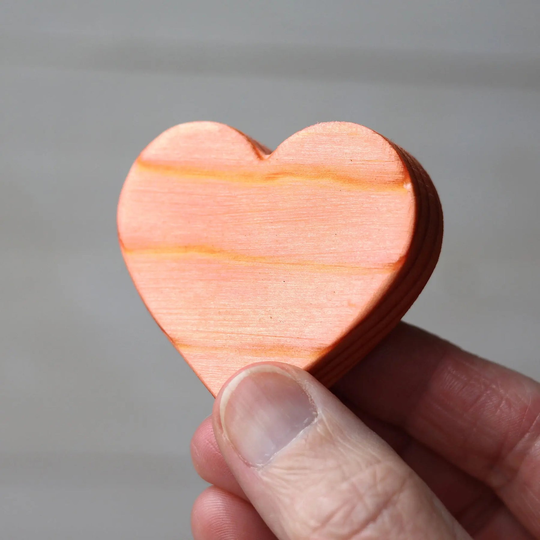 Hand holding a small wooden heart with wood grain and orange tones.
