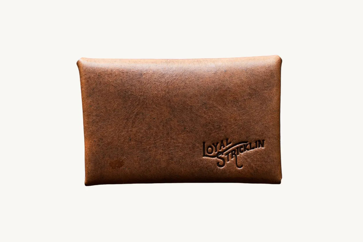 Cognac leather envelope wallet with 'Loyal Stricklin' logo detail on back. Minimalist style.