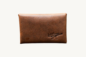 Cognac leather envelope wallet with 'Loyal Stricklin' logo detail on back. Minimalist style.