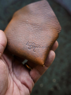 Cognac brown leather wallet with embossed logo in hand, showing texture and color.
