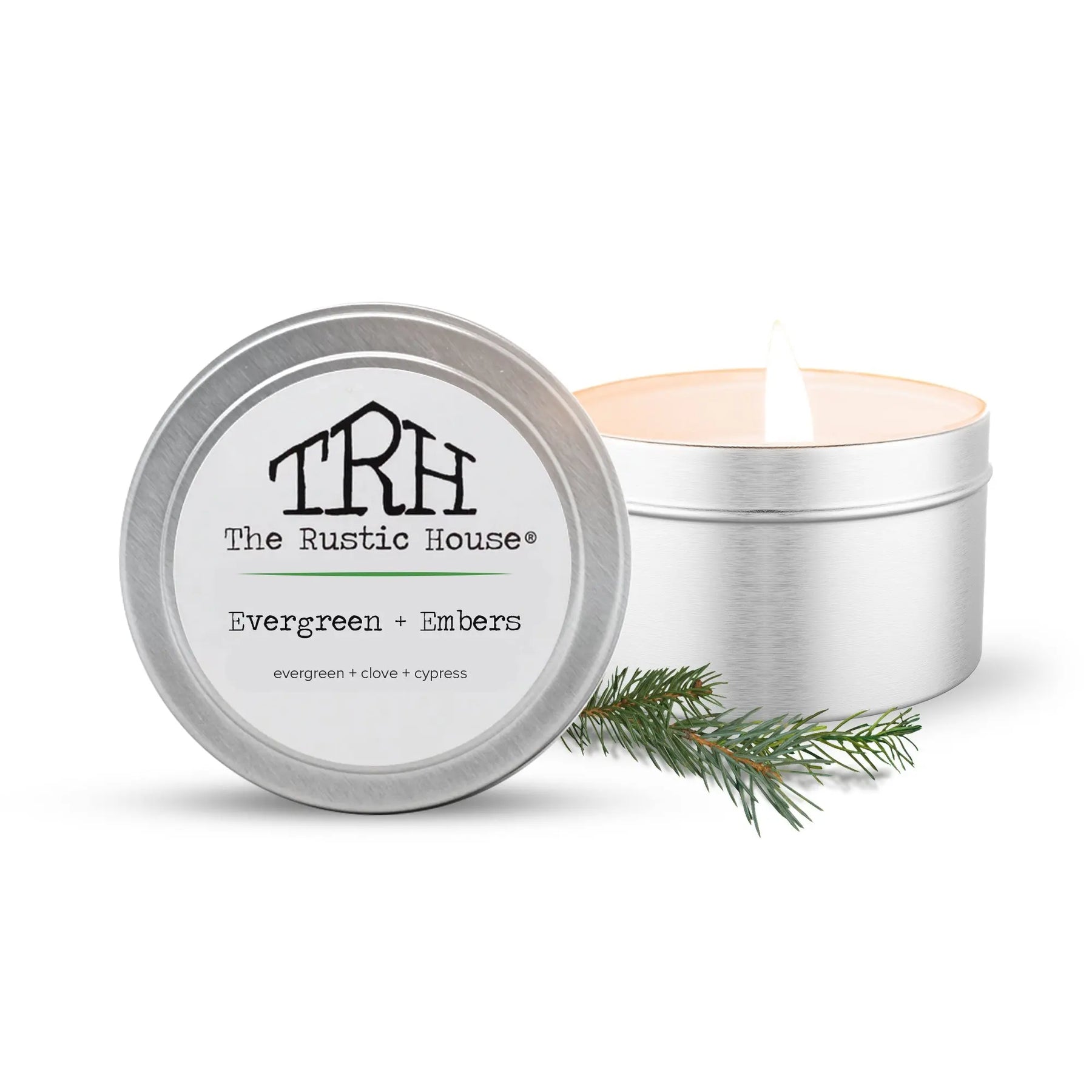 The Rustic House Evergreen + Embers travel tin candle with burning flame and pine sprig.