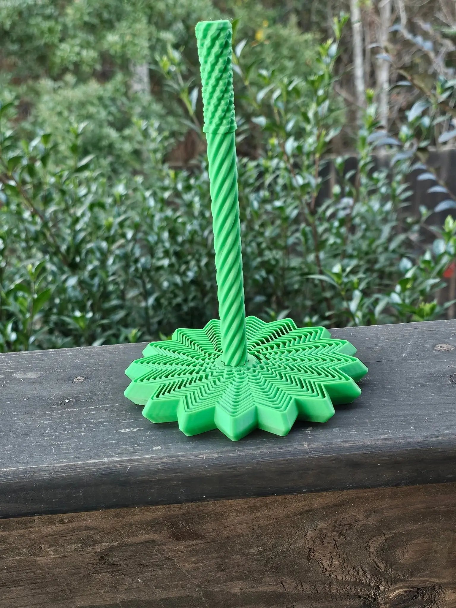 Green 3D printed fidget spinner with a twisting center post and star-shaped base, sitting on a wooden surface.