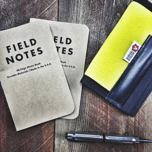 Field Notes notebooks and a pen on a wooden surface, with a yellow canvas item.