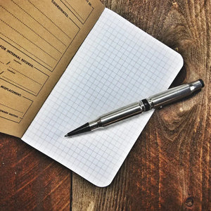 Open Field Notes graph paper notebook with a bullet-shaped pen on a wooden background.