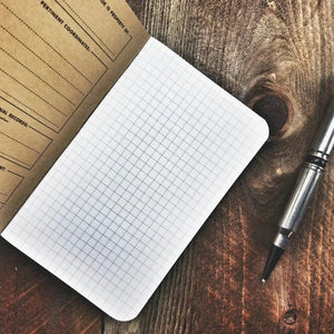 Open Field Notes graph paper notebook with a pen on a wooden table