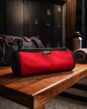 Red fire hose dopp kit with black trim and logo on a wooden surface.