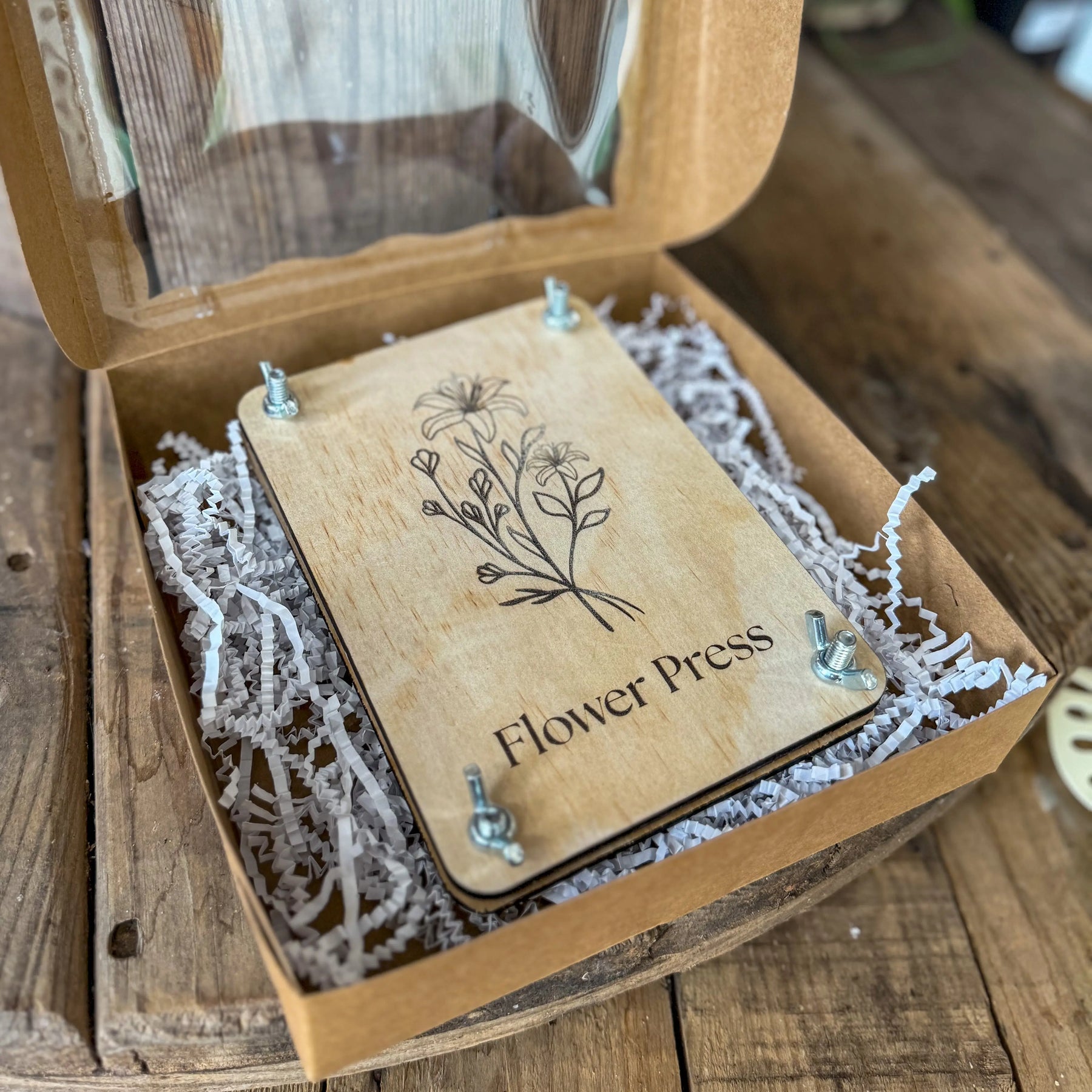 Wooden flower press with floral engraving and metal wing nuts in a box