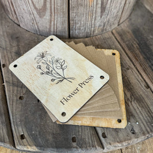 Wooden flower press with floral design and paper sheets on a wooden spool.