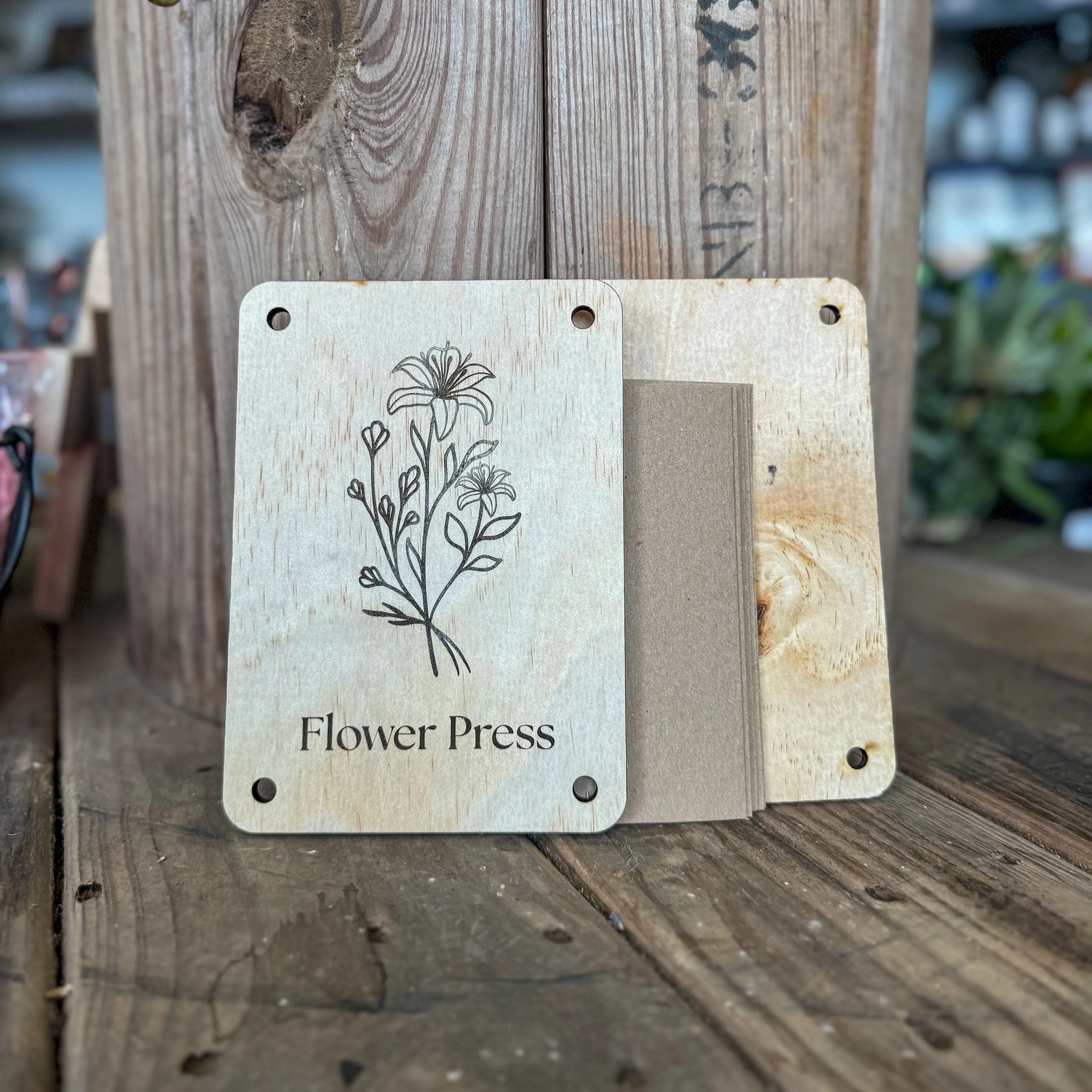 Wooden flower press with floral engraving and cards on a rustic table.