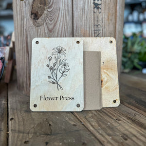 Wooden flower press with floral engraving and cards on a rustic table.