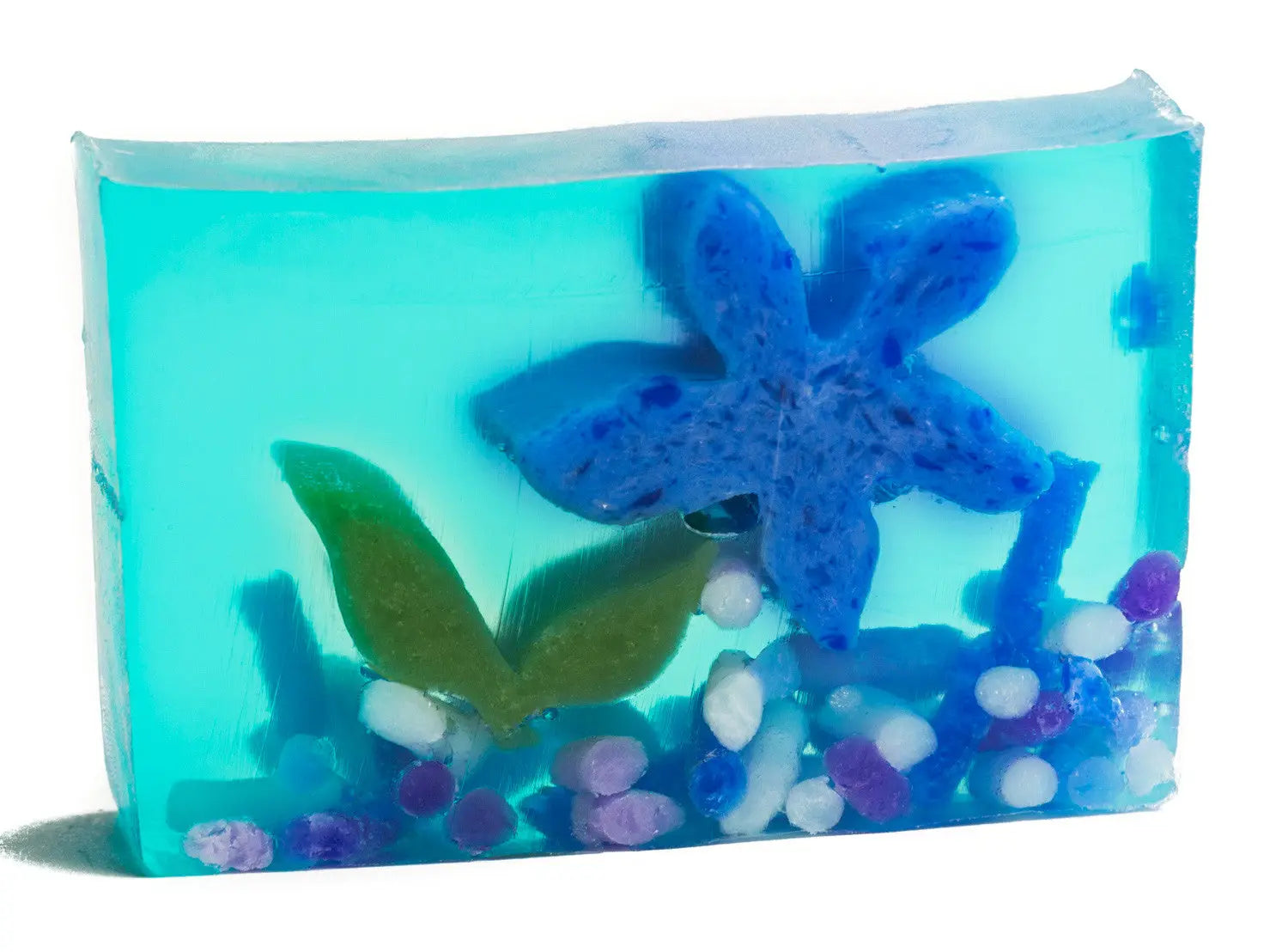 Blue transparent soap slice with embedded blue starfish, green leaves, and colorful pebbles.