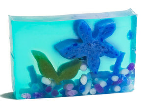 Blue transparent soap slice with embedded blue starfish, green leaves, and colorful pebbles.