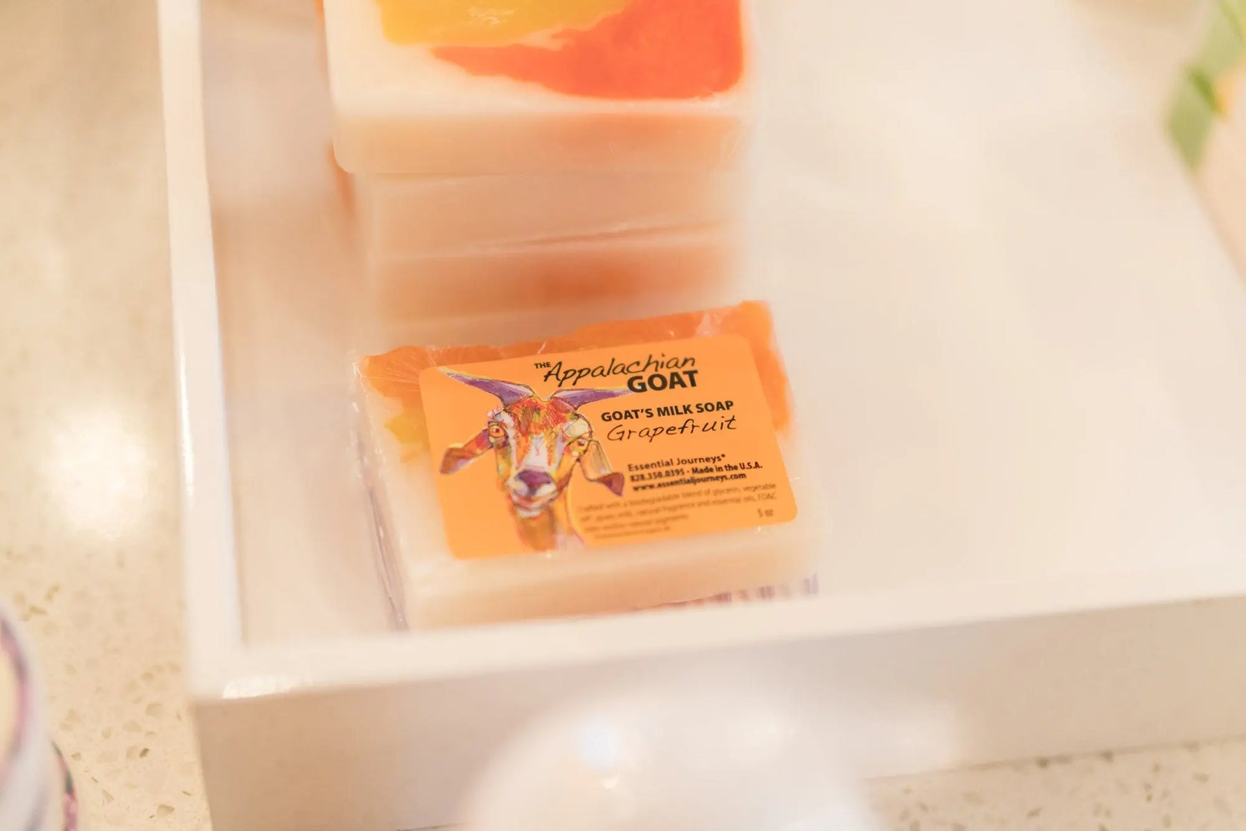 Grapefruit goat milk soap bar with orange and pink swirls on a white tray.