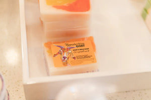 Grapefruit goat milk soap bar with orange and pink swirls on a white tray.