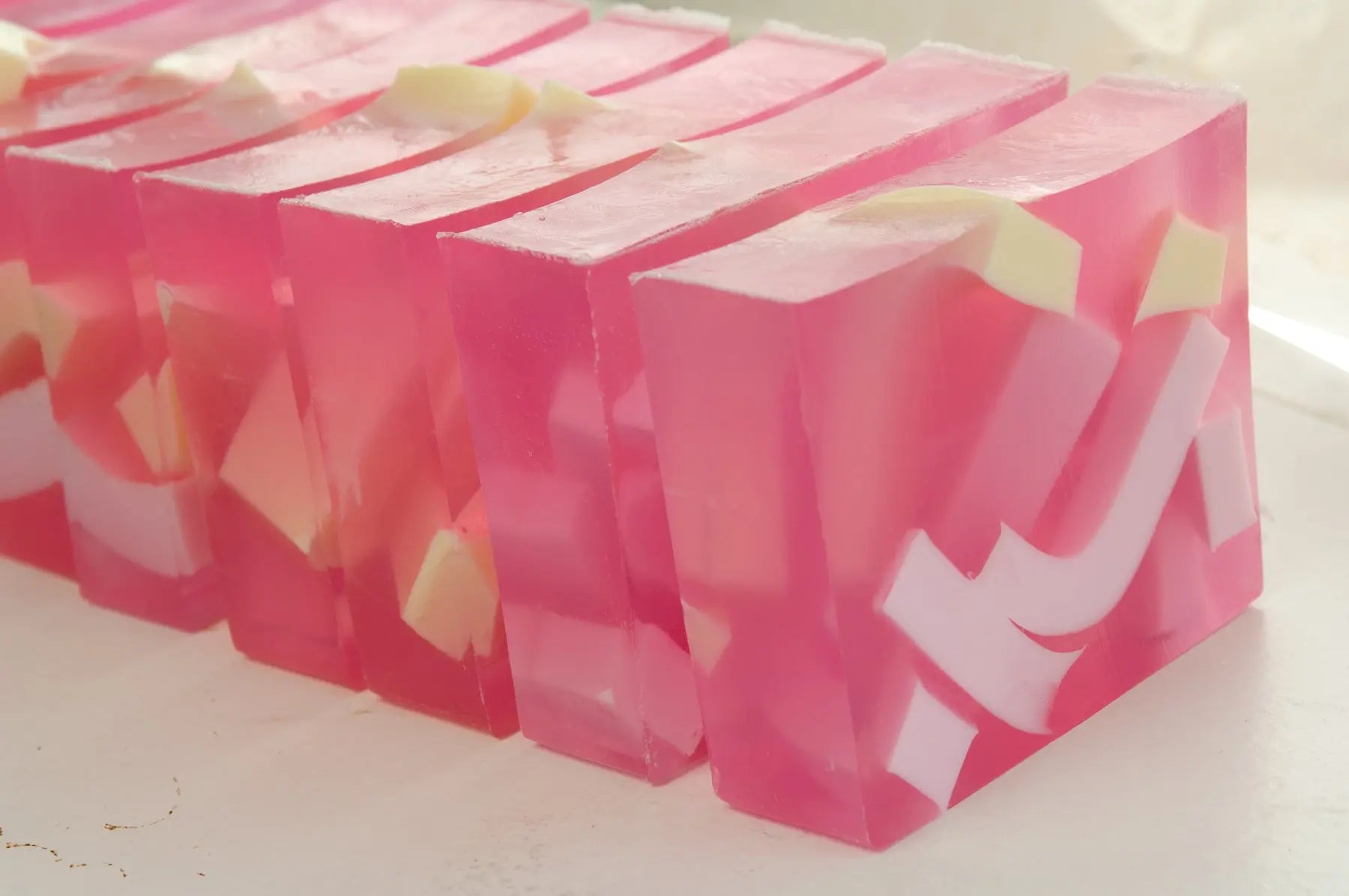 Pink translucent soap slices with white and yellow pieces embedded inside, arranged in a row.