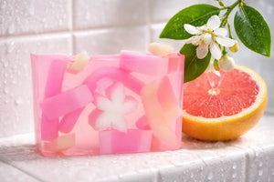 Pink translucent soap slice with white flower and fruit inclusions next to grapefruit half.