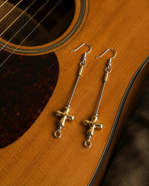 Gold cross earrings on a wooden acoustic guitar