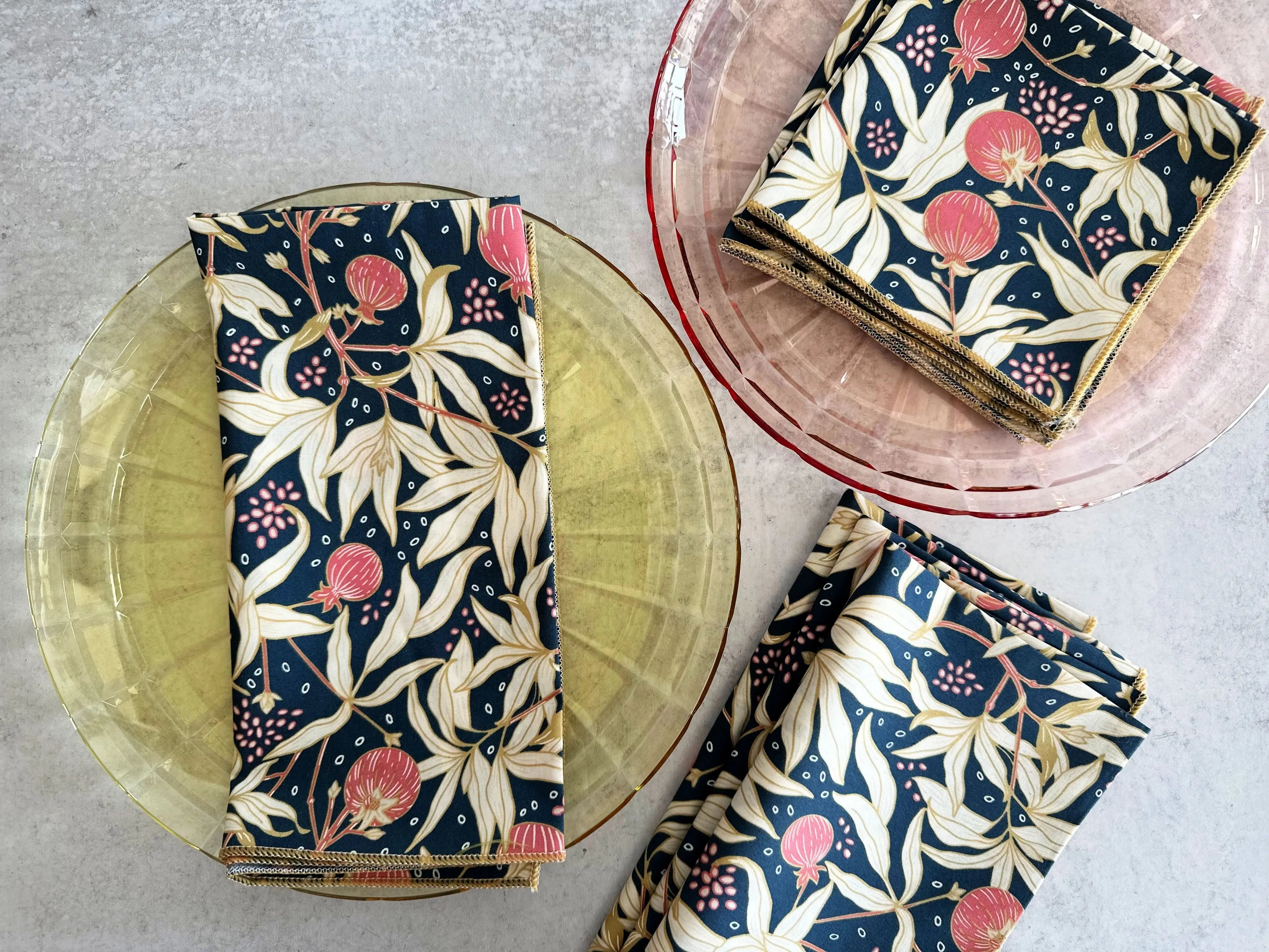 Four navy blue cloth napkins with a floral pattern featuring pink fruits and cream leaves.