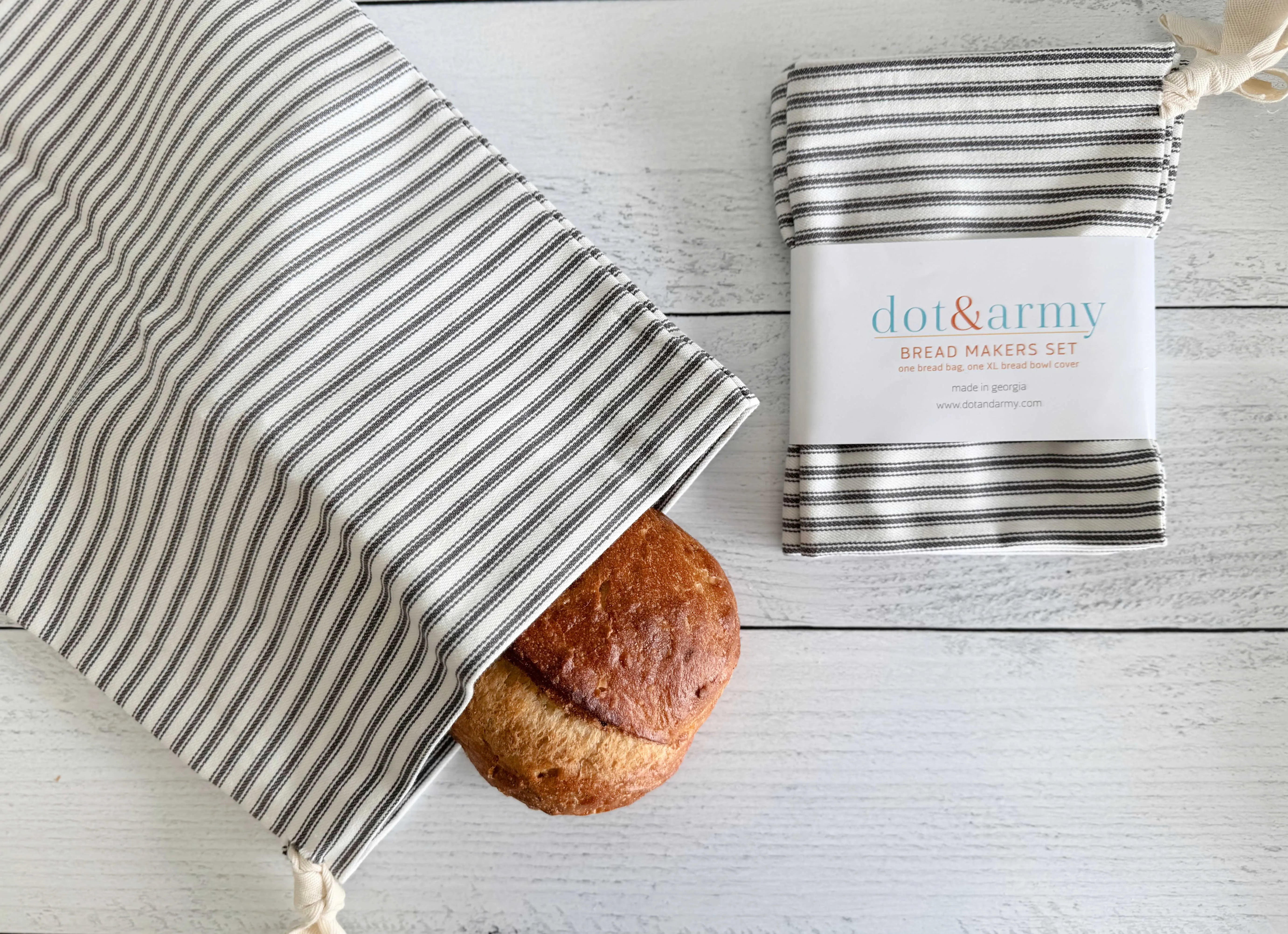 Two striped fabric bread bags with one loaf of bread and product packaging.
