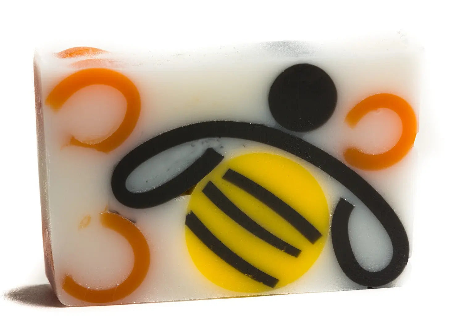White soap slice with honey bee design: black swirls, yellow circle with stripes, orange rings.