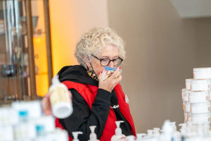 Woman in red vest smelling a bar of honeysuckle goat's milk soap in a shop.