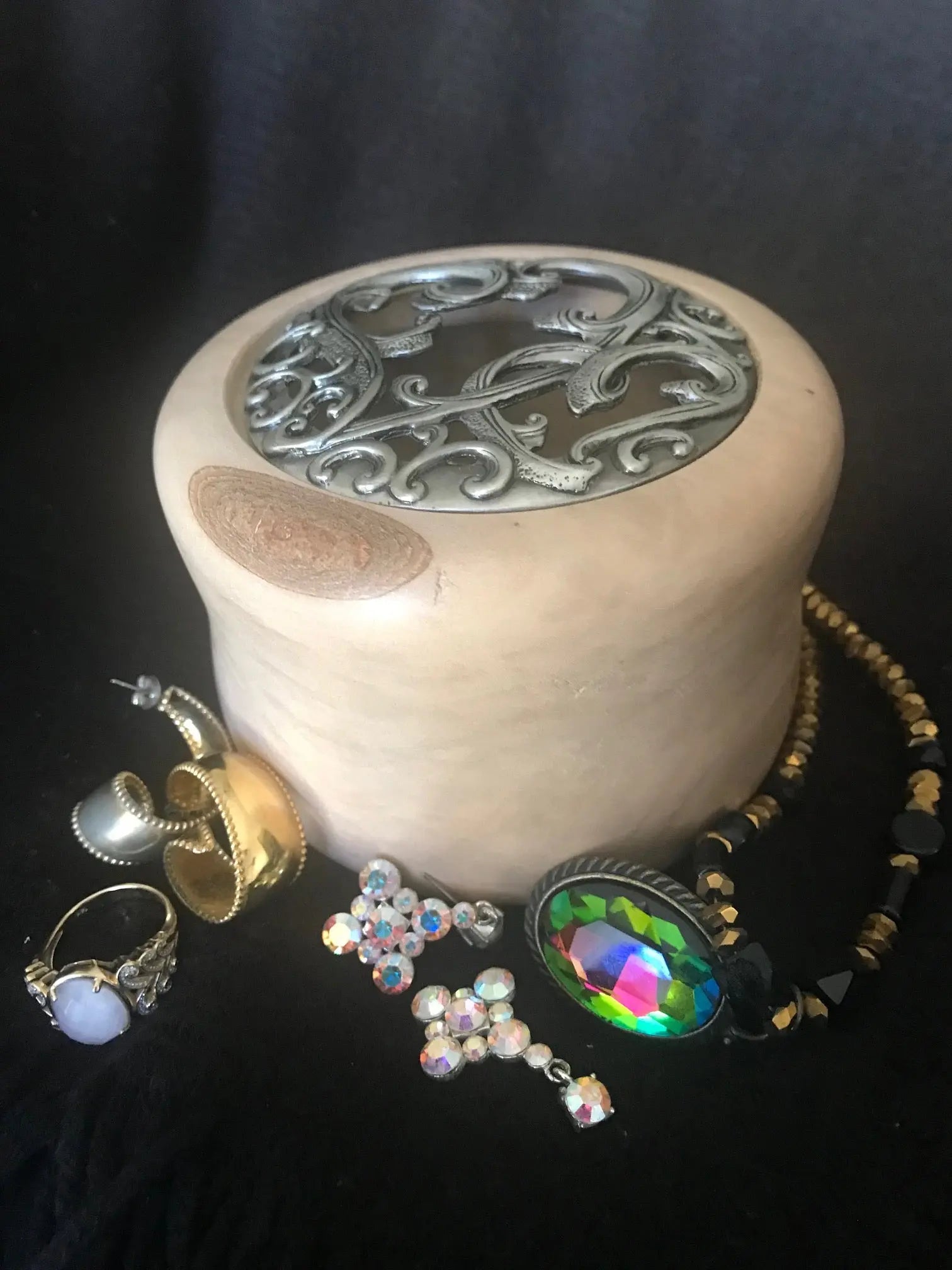 River Birch treasure box with metal filigree lid surrounded by rings, earrings, and beaded necklace on a black background.