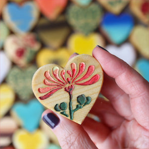 Hand holding heart-shaped cookie with flower design, colorful hearts background.