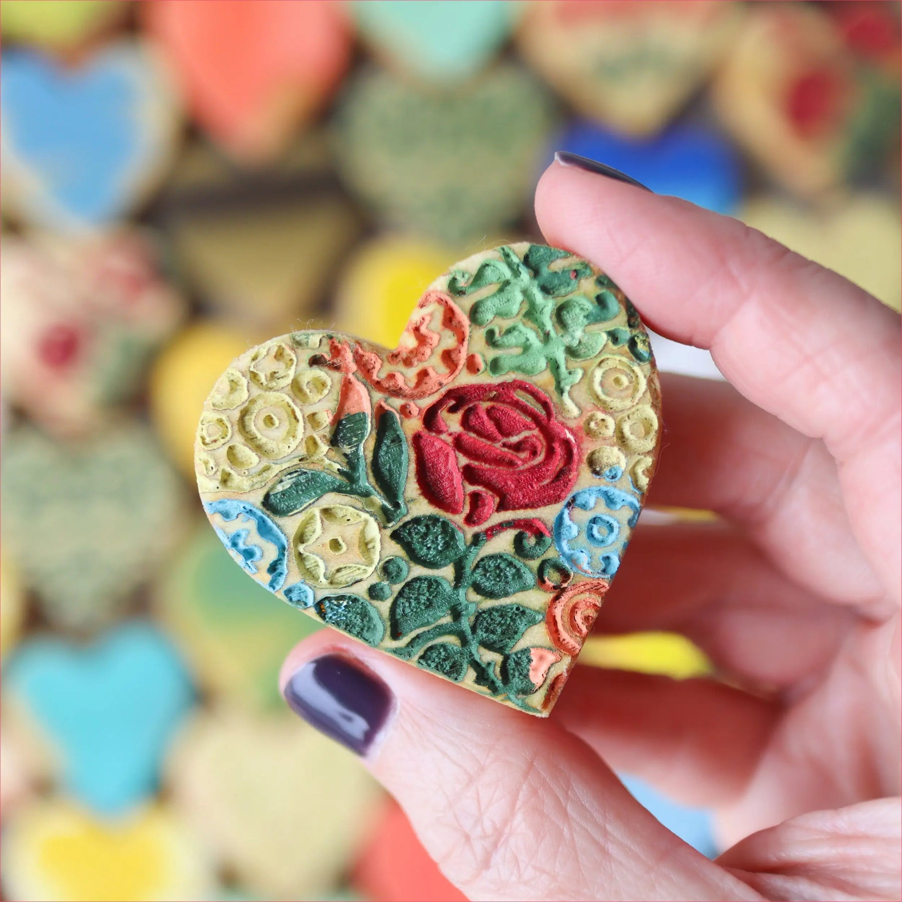 Hand holding a colorful heart-shaped item with raised floral patterns.