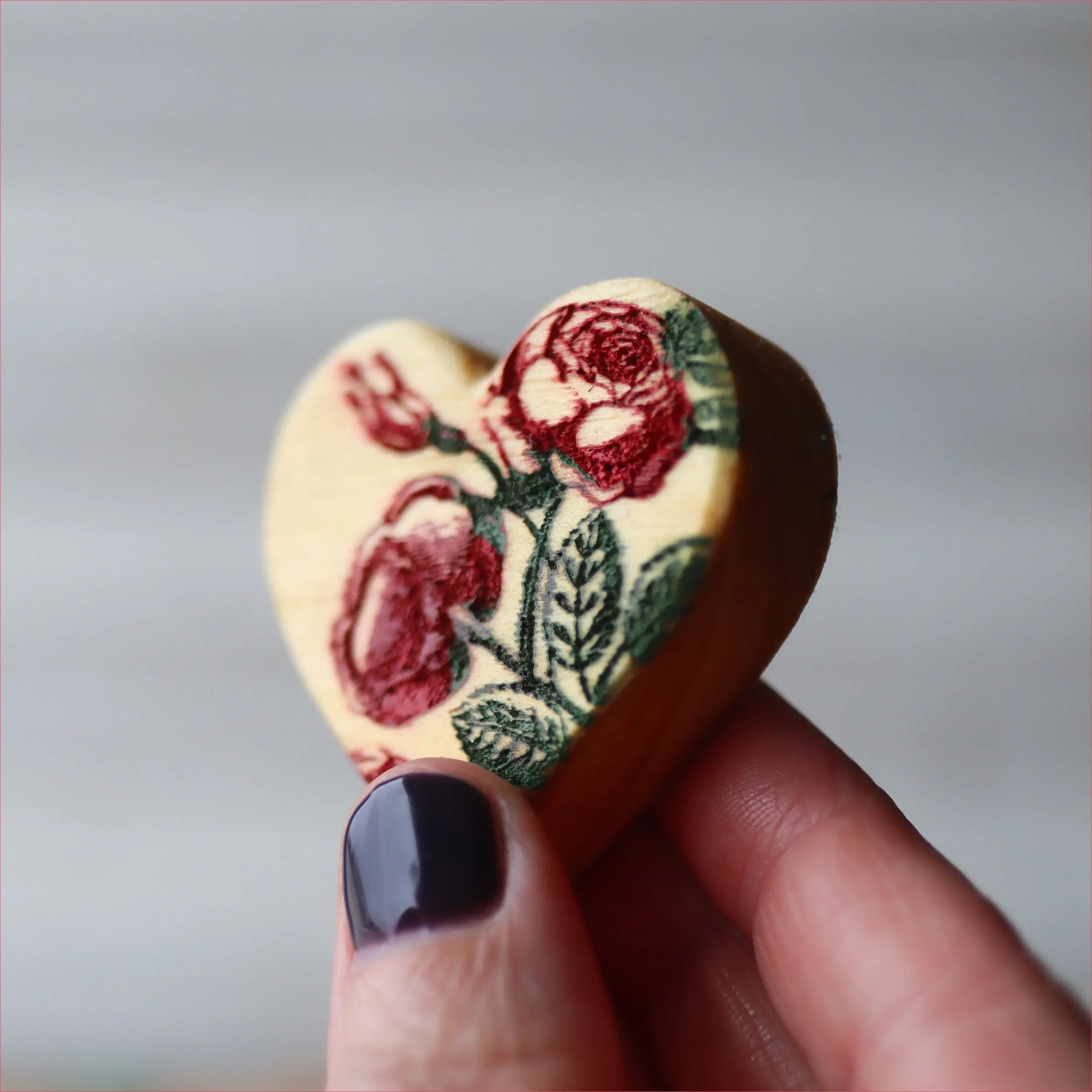 Heart-shaped wooden object with red rose floral print held by fingers