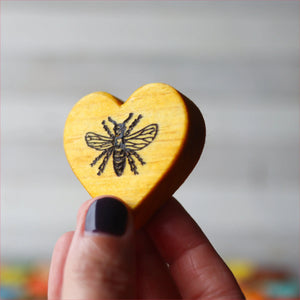 Hand holding a wooden heart with a bee engraving.