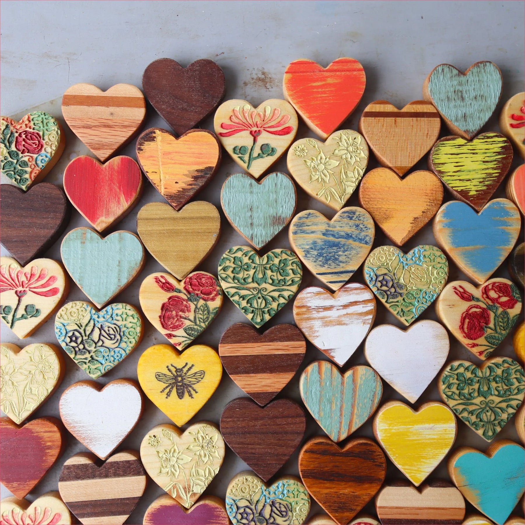 Many small wooden hearts with painted and carved designs arranged on a surface.