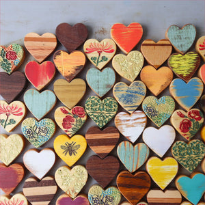 Many small wooden hearts with painted and carved designs arranged on a surface.