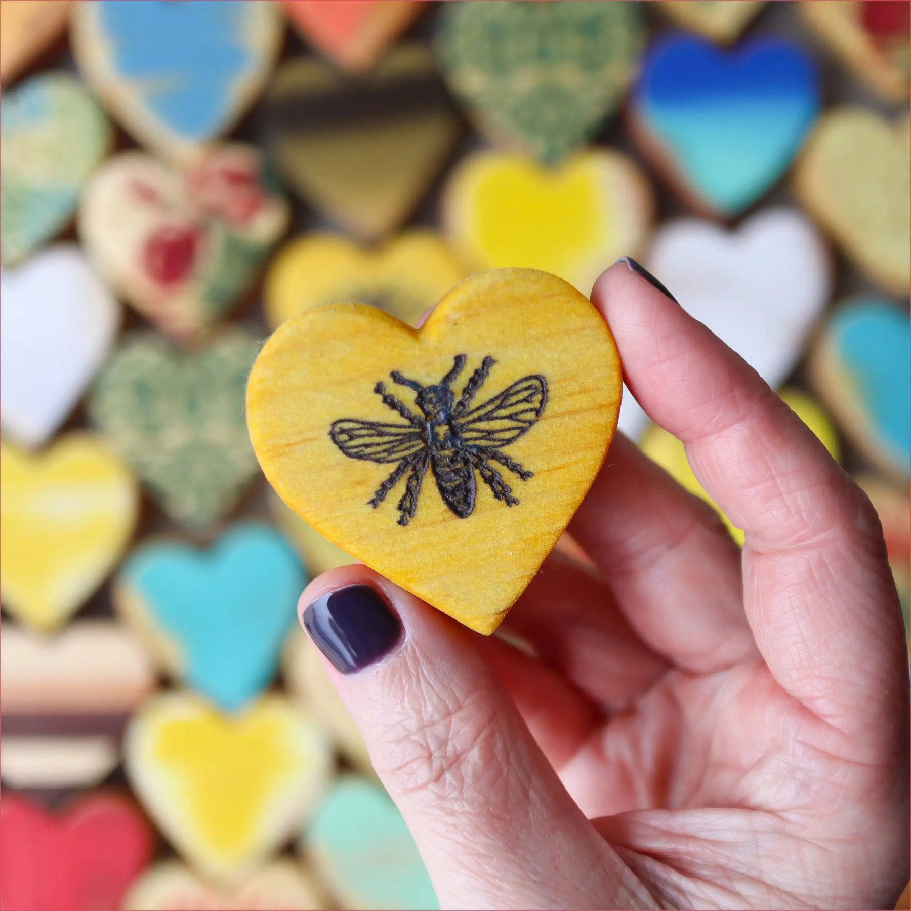 Yellow heart cookie with a black bee design, blurred heart cookies in background.