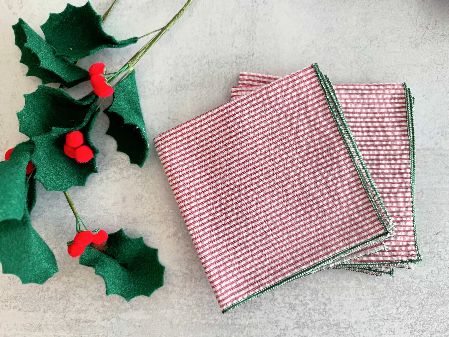Christmas holly leaves with red berries and red and white striped napkins with green trim.