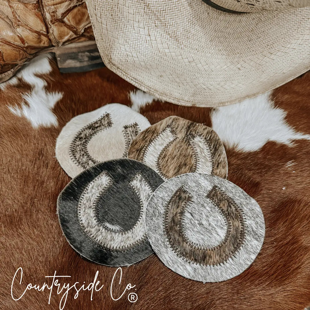 Set of 4 cowhide horseshoe coasters on a brown and white spotted hide.