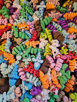 Pile of colorful 3D printed articulated fidget toys featuring animals, monsters, and other unique designs.