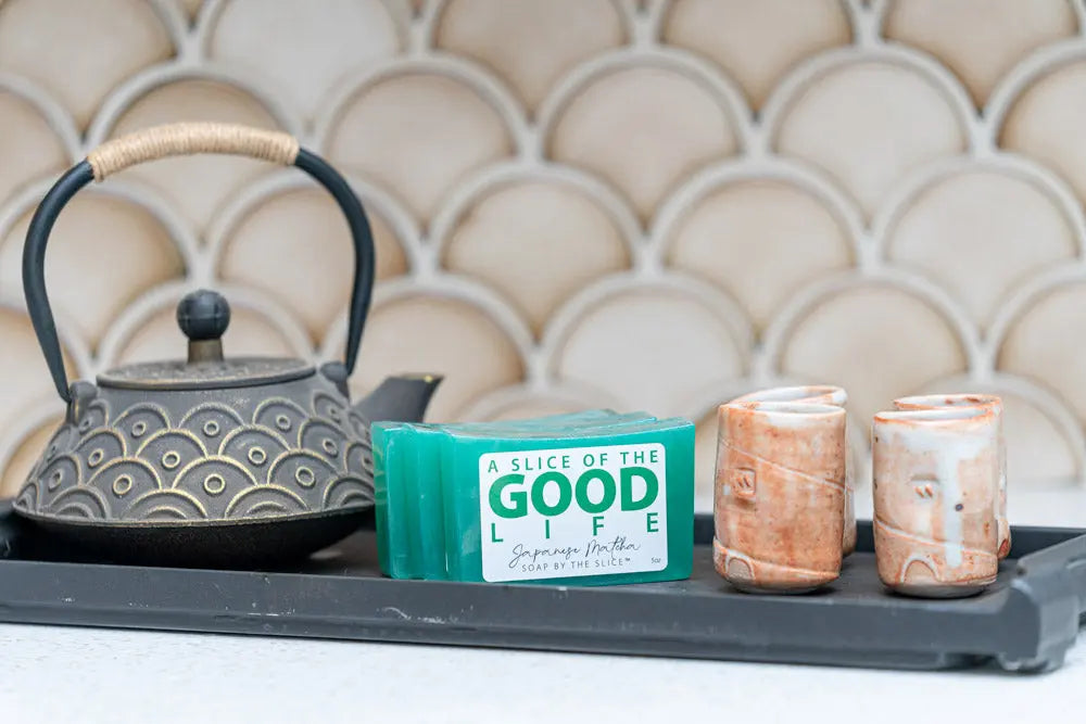 Japanese Matcha soap slices with a small cast iron teapot and ceramic cups on a dark tray.